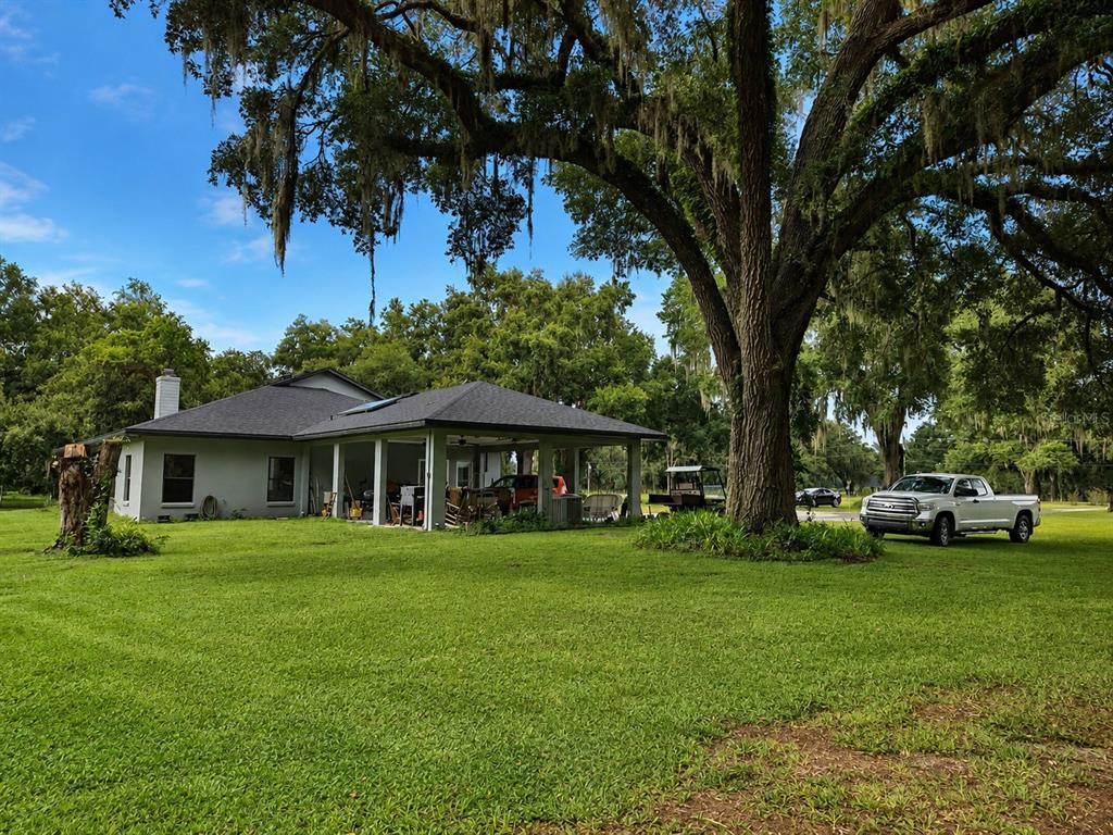 A large, open-sided metal pole barn structure sits on a grassy lot under trees — 2672 SE 35TH STREET, SUMTERVILLE, FL