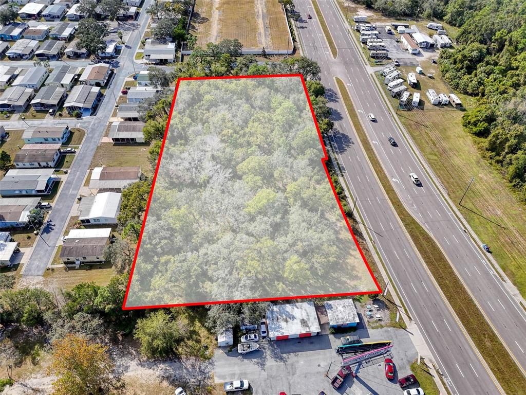 An aerial view shows a wooded, trapezoidal lot outlined in red next to a highway — 10780 STATE ROAD 52, HUDSON, FL