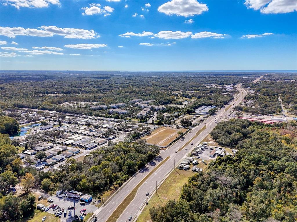 An aerial view shows a multi-lane highway running through a wooded area with residential developments — 10780 STATE ROAD 52, HUDSON, FL