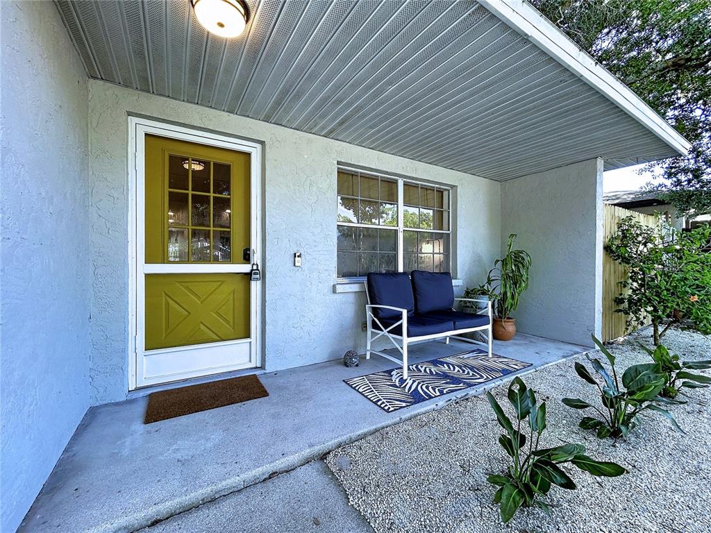 A front porch features a yellow door, a blue loveseat, and a gravel garden bed — 815 35TH STREET W, BRADENTON, FL