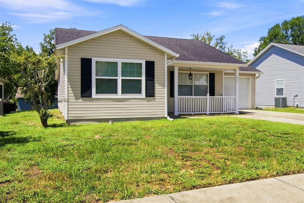 A single-story house with beige vinyl siding, black shutters, and a small front porch — 863 WISTERIA PLACE, TAVARES, FL