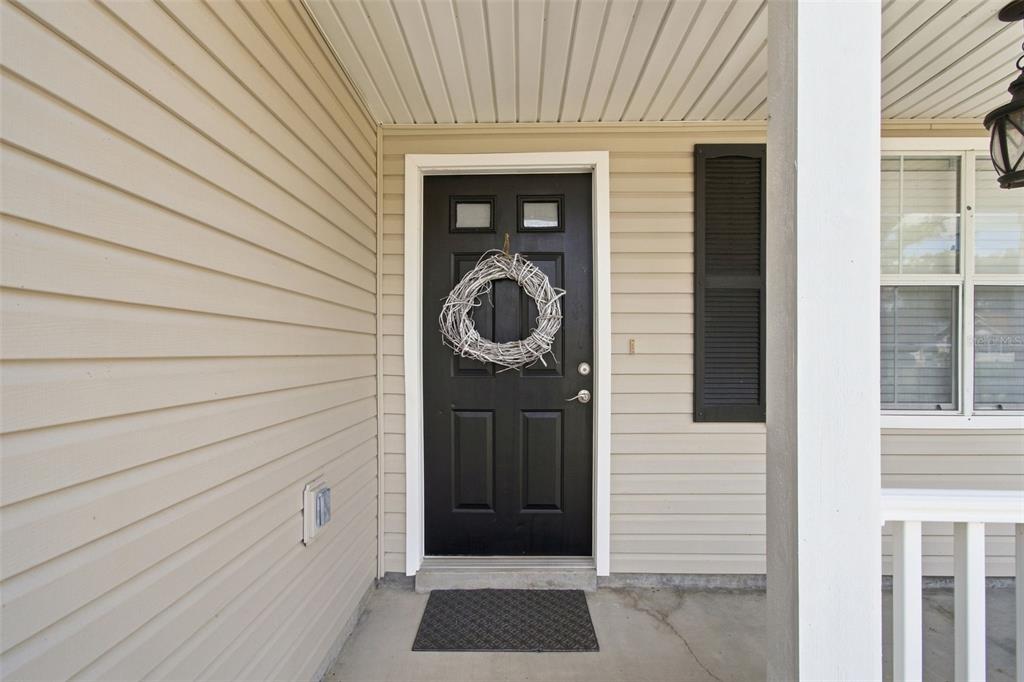 A black front door with a wreath sits on a porch with beige vinyl siding — 863 WISTERIA PLACE, TAVARES, FL