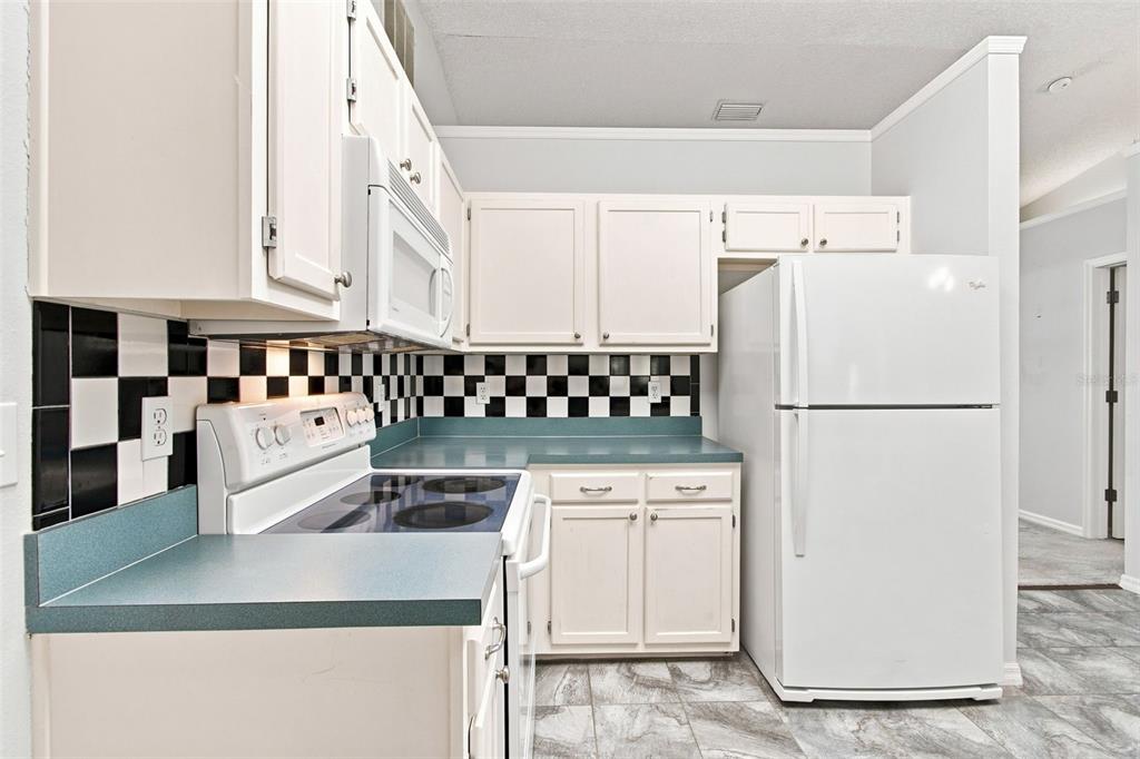A kitchen features white cabinets, a teal countertop, a black-and-white checkered backsplash, and white appliances — 863 WISTERIA PLACE, TAVARES, FL