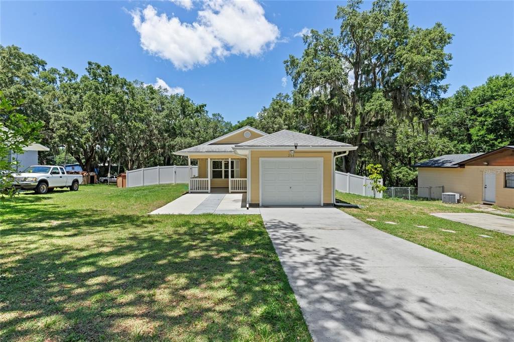 A tan house exterior features a covered porch with white railings and a concrete walkway — 206 E CATAWBA, FRUITLAND PARK, FL