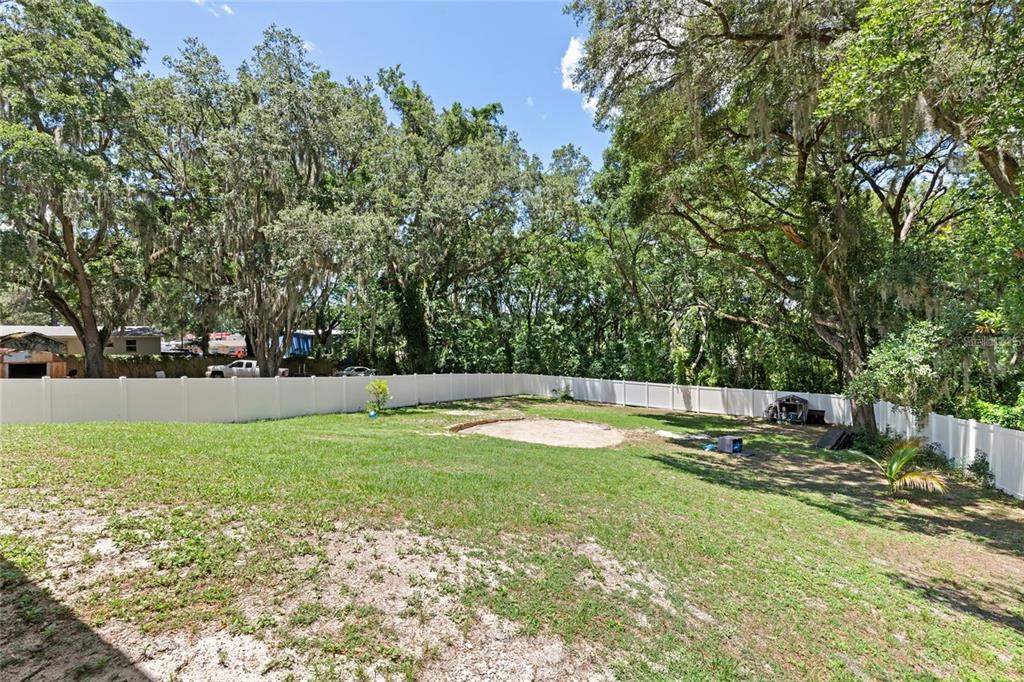A fenced backyard features a grassy lawn, a circular sandy area, and mature oak trees — 206 E CATAWBA, FRUITLAND PARK, FL