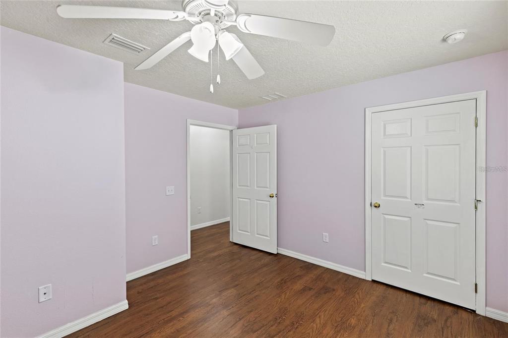A bedroom with light purple walls, wood-look flooring, a ceiling fan, and two white doors — 206 E CATAWBA, FRUITLAND PARK, FL