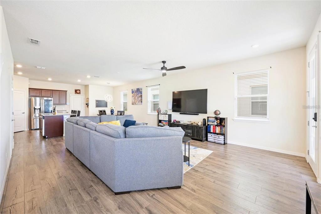A spacious living room with wood-look flooring, a large sectional sofa, and an open kitchen — 2769 FRANKLIN ROAD, ST CLOUD, FL