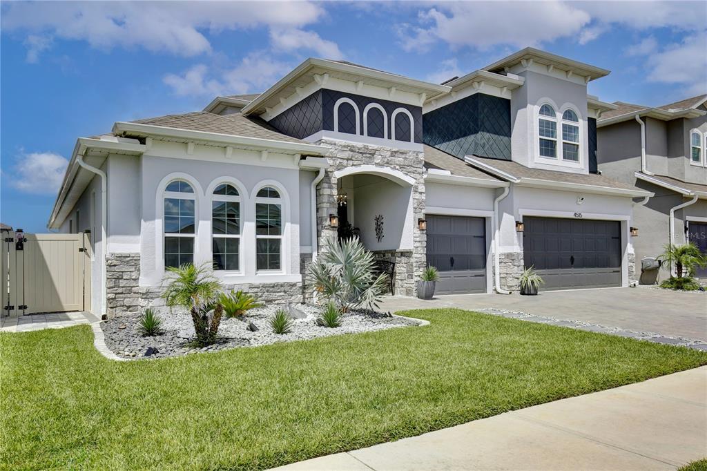 A two-story suburban house with a stone facade, arched windows, and a three-car garage — 4515 LIONS GATE AVENUE, CLERMONT, FL
