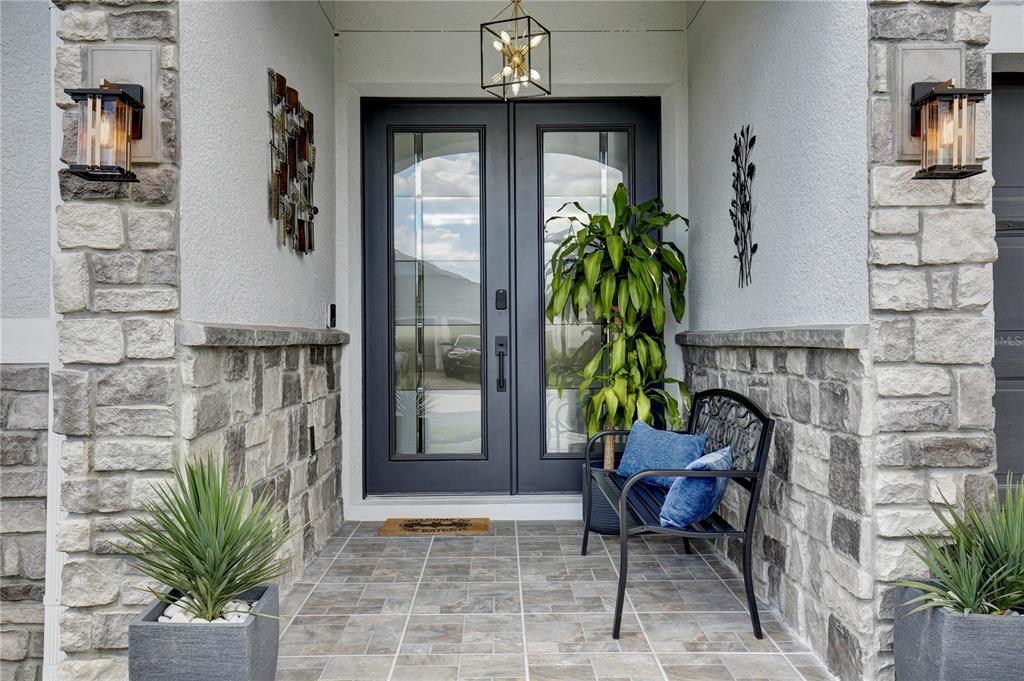 A covered entryway features a double front door, stone siding, tile flooring, and a metal bench — 4515 LIONS GATE AVENUE, CLERMONT, FL