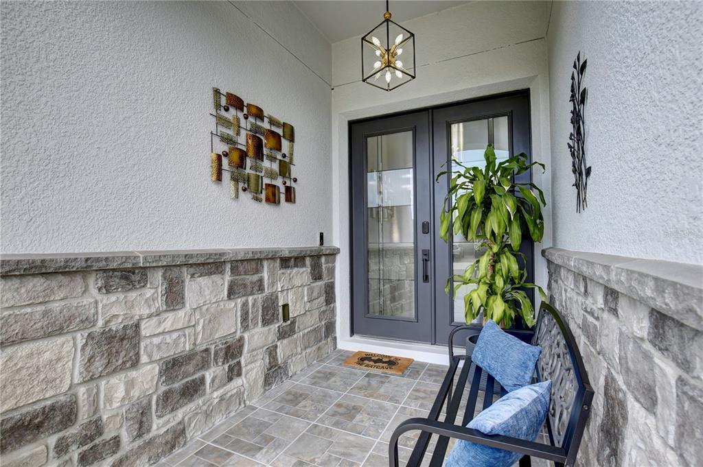 A covered entryway features a stone-accented wall, a dark double door, and a metal bench — 4515 LIONS GATE AVENUE, CLERMONT, FL