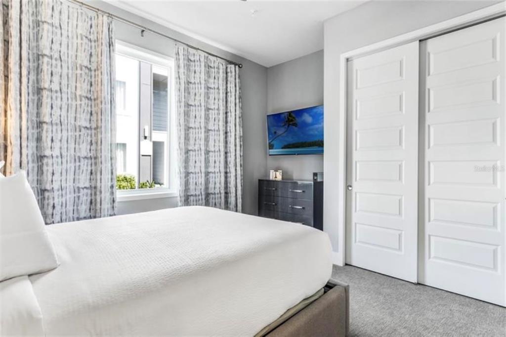 A bedroom features a bed, a wall-mounted television, a dresser, and white sliding closet doors — 7760 SANDY RIDGE DRIVE UNIT 108, REUNION, FL