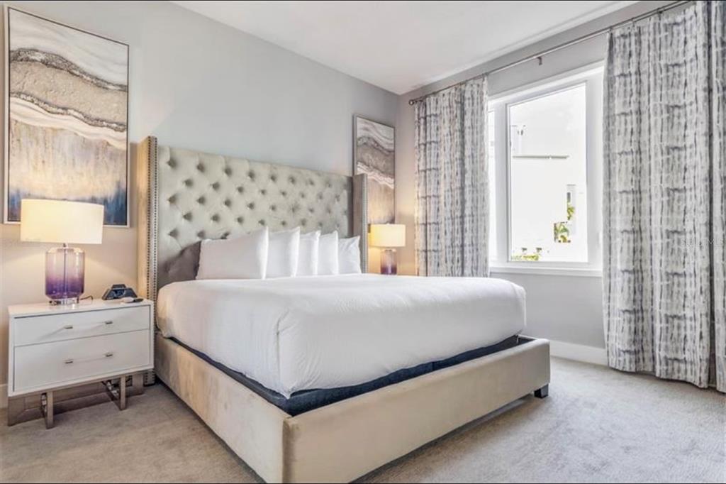 A bedroom features a tufted beige headboard, white bedding, two nightstands, and patterned floor-length curtains — 7760 SANDY RIDGE DRIVE UNIT 108, REUNION, FL