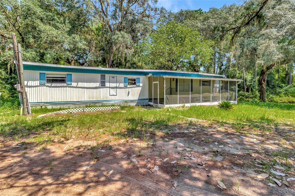 A single-story mobile home with blue shutters and a screened-in porch sits on a grassy lot — 110 HOLLISTER SCHOOL ROAD, PALATKA, FL