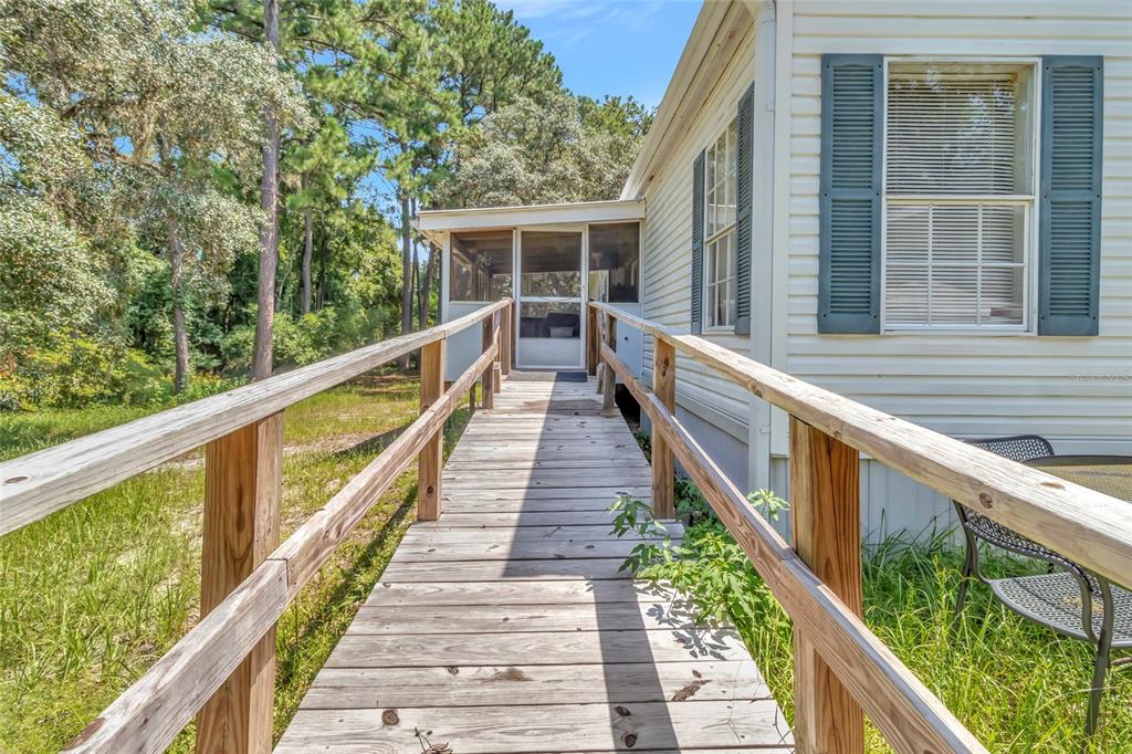 A wooden wheelchair ramp leads to the screened-in porch of a light-colored mobile home — 110 HOLLISTER SCHOOL ROAD, PALATKA, FL