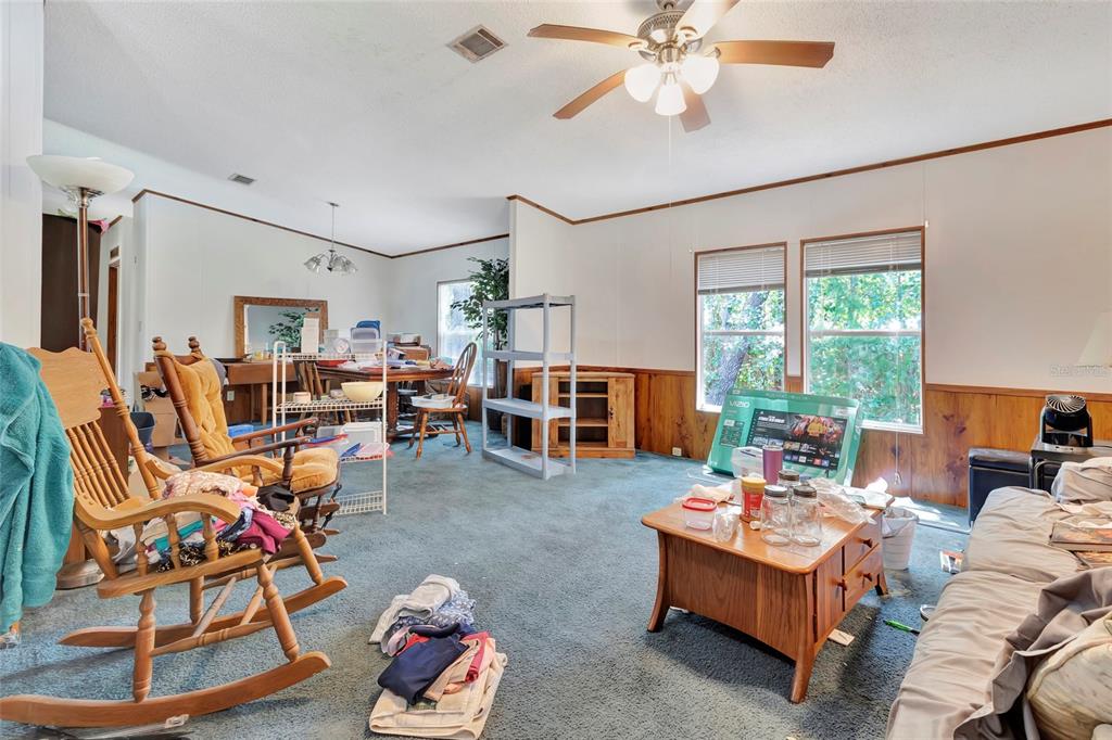 A living room with blue carpeting, wood paneling, a ceiling fan, and a wooden coffee table — 110 HOLLISTER SCHOOL ROAD, PALATKA, FL