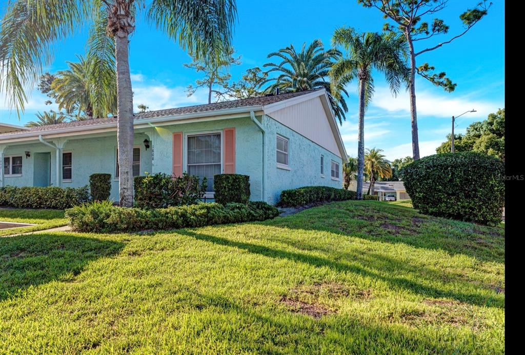 A light green single-story building with a carport and palm trees on a sunny day — 2465 NORTHSIDE DRIVE UNIT 1808, CLEARWATER, FL