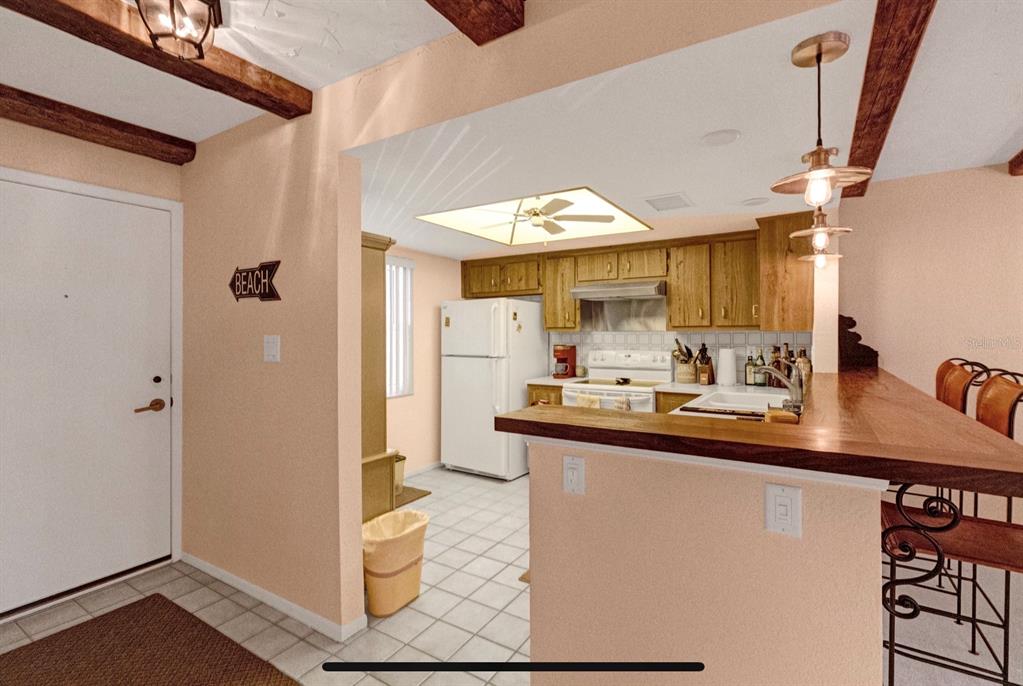A kitchen features wood cabinets, white appliances, a tiled floor, and a breakfast bar — 2465 NORTHSIDE DRIVE UNIT 1808, CLEARWATER, FL
