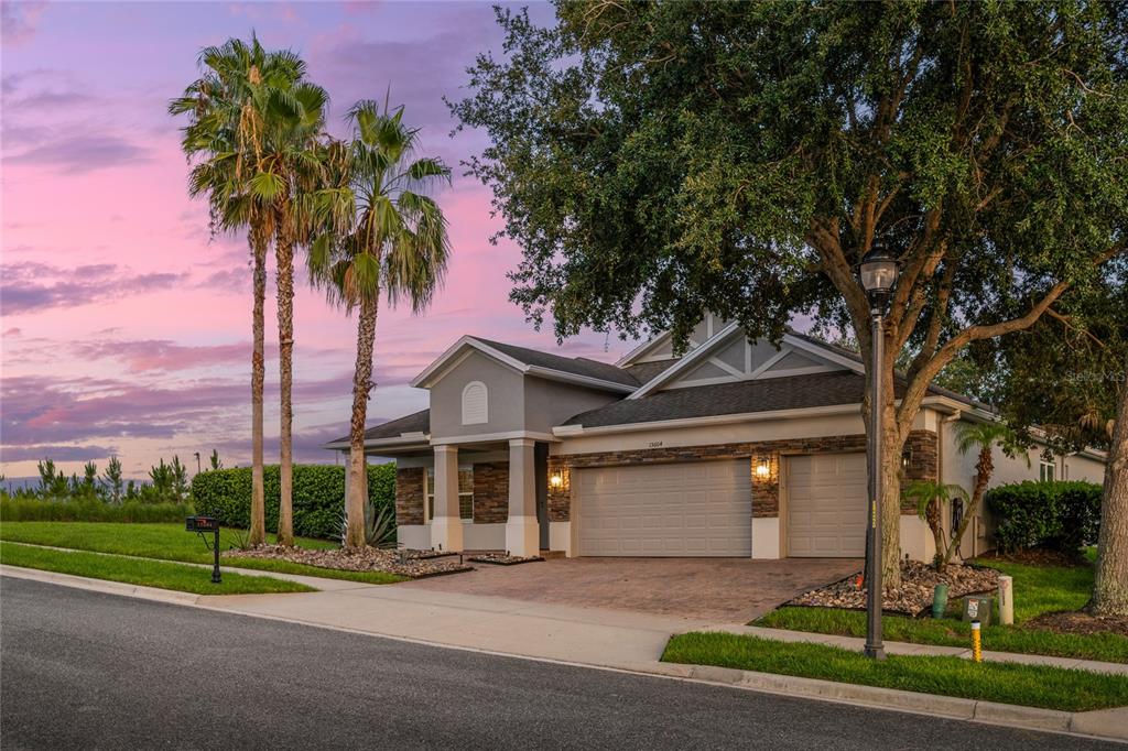 A single-story house with a stone facade, two-car garage, and palm trees at dusk — 15604 GRANLUND STREET, WINTER GARDEN, FL