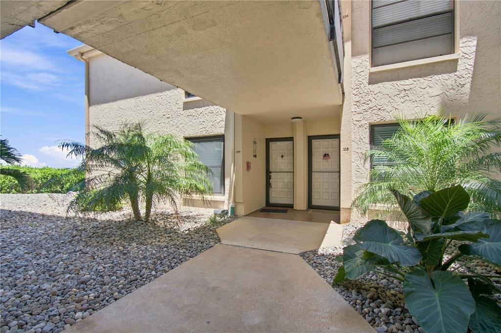 A concrete walkway leads to two adjacent apartment entrances under a covered building overhang — 6177 SUN BOULEVARD UNIT 109, ST PETERSBURG, FL