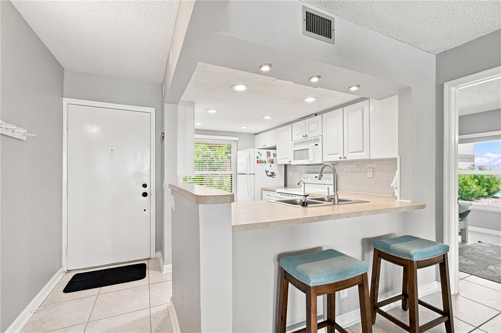 A kitchen with white cabinets, a breakfast bar, and two stools near an entryway — 6177 SUN BOULEVARD UNIT 109, ST PETERSBURG, FL