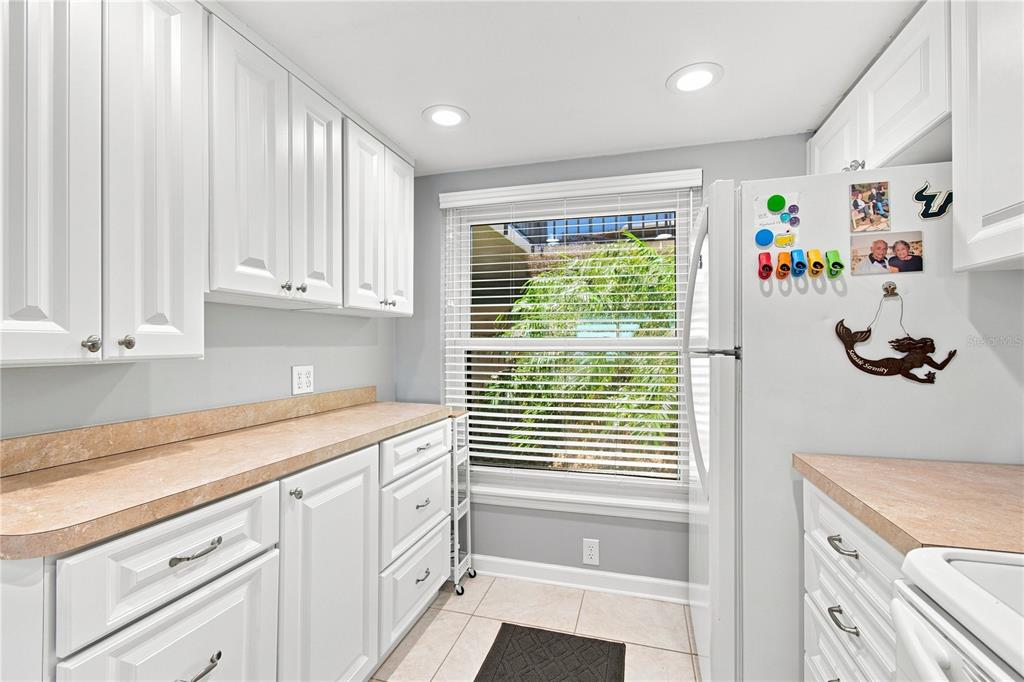 A white kitchen features light-colored countertops, white cabinetry, a window with blinds, and a refrigerator — 6177 SUN BOULEVARD UNIT 109, ST PETERSBURG, FL