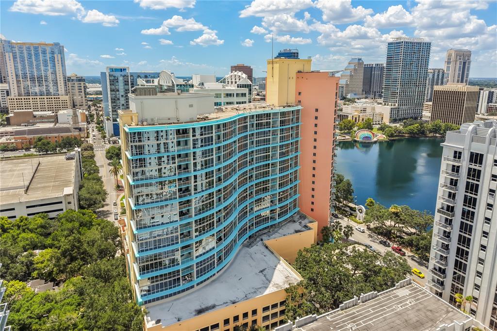 An aerial view shows a curved, blue-glass residential tower next to a lake in a city — 322 E CENTRAL BOULEVARD UNIT 1910, ORLANDO, FL