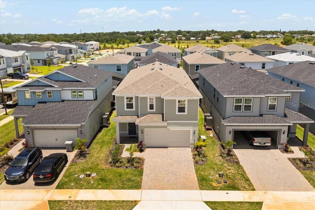 An aerial view shows a suburban street with three two-story houses and paved driveways — 15952 CAPE CORAL LOOP, CLERMONT, FL
