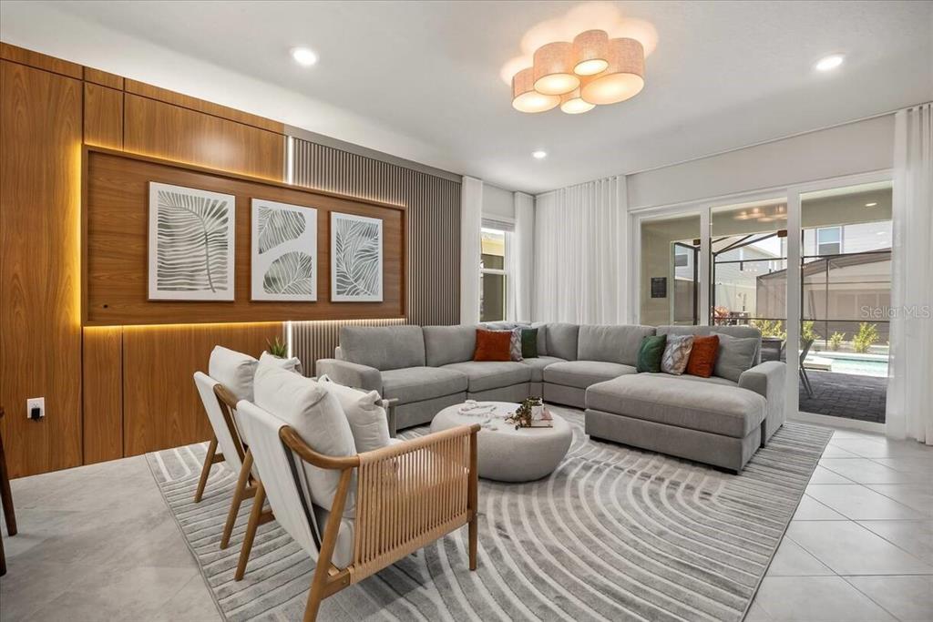 A modern living room features a grey sectional sofa, two wooden chairs, and wood-paneled walls — 15952 CAPE CORAL LOOP, CLERMONT, FL