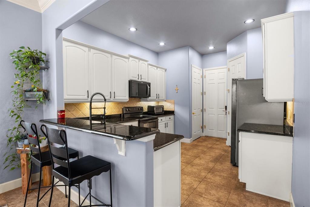 A kitchen features white cabinets, black countertops, a breakfast bar, and light blue walls — 1445 FAIRVIEW CIRCLE, KISSIMMEE, FL