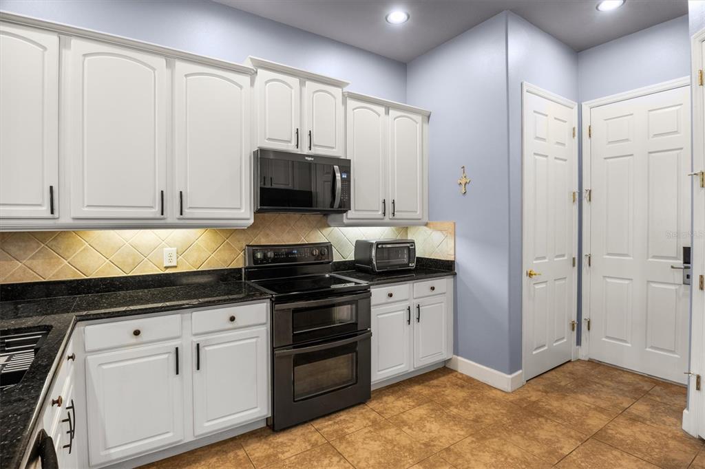 A kitchen features white cabinets, black countertops, a black oven, and light blue walls — 1445 FAIRVIEW CIRCLE, KISSIMMEE, FL
