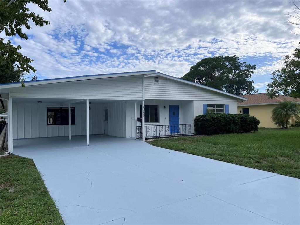 A single-story house features a light blue painted driveway, a carport, and a blue front door — 3602 17TH AVENUE W, BRADENTON, FL