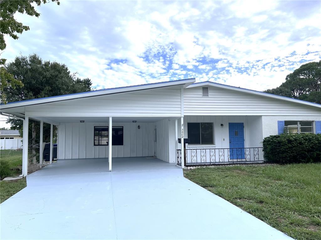 A single-story house features a white exterior, a blue front door, and an attached carport — 3602 17TH AVENUE W, BRADENTON, FL