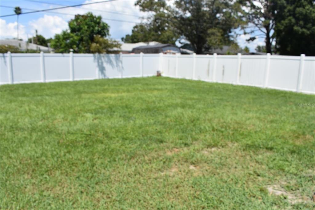 A grassy backyard is enclosed by a white vinyl privacy fence under a blue sky — 3602 17TH AVENUE W, BRADENTON, FL