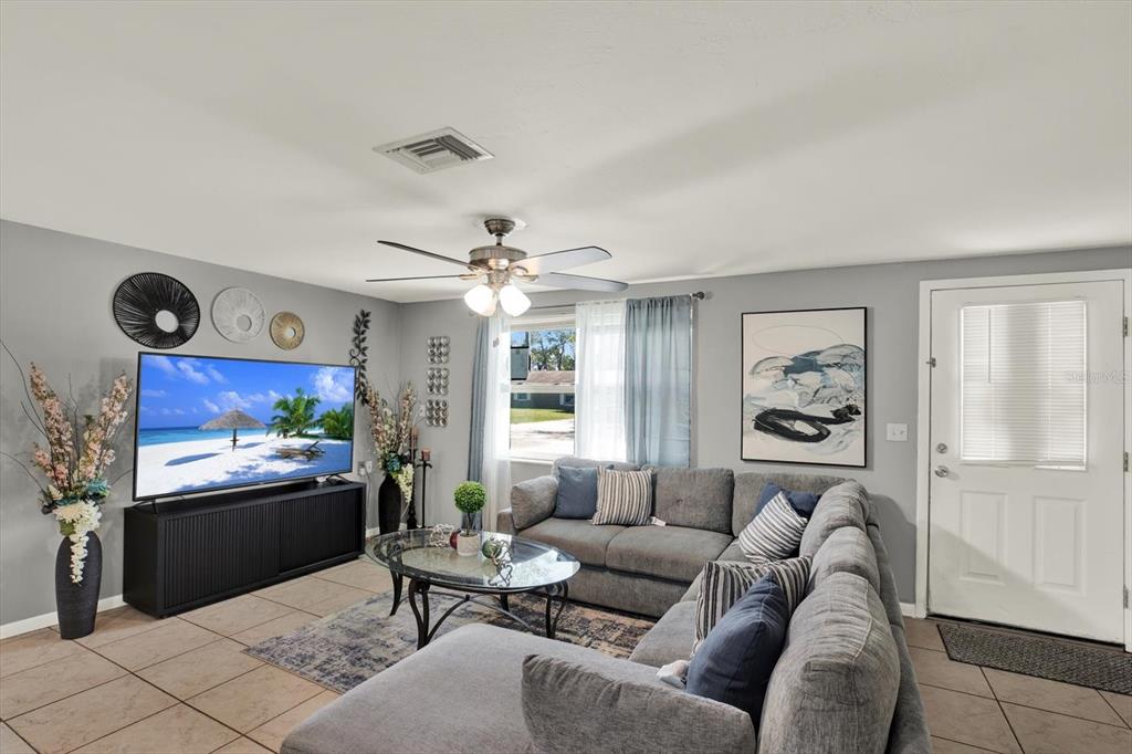 A living room features a grey sectional sofa, a television, and a glass coffee table — 5609 QUIST DRIVE, PORT RICHEY, FL