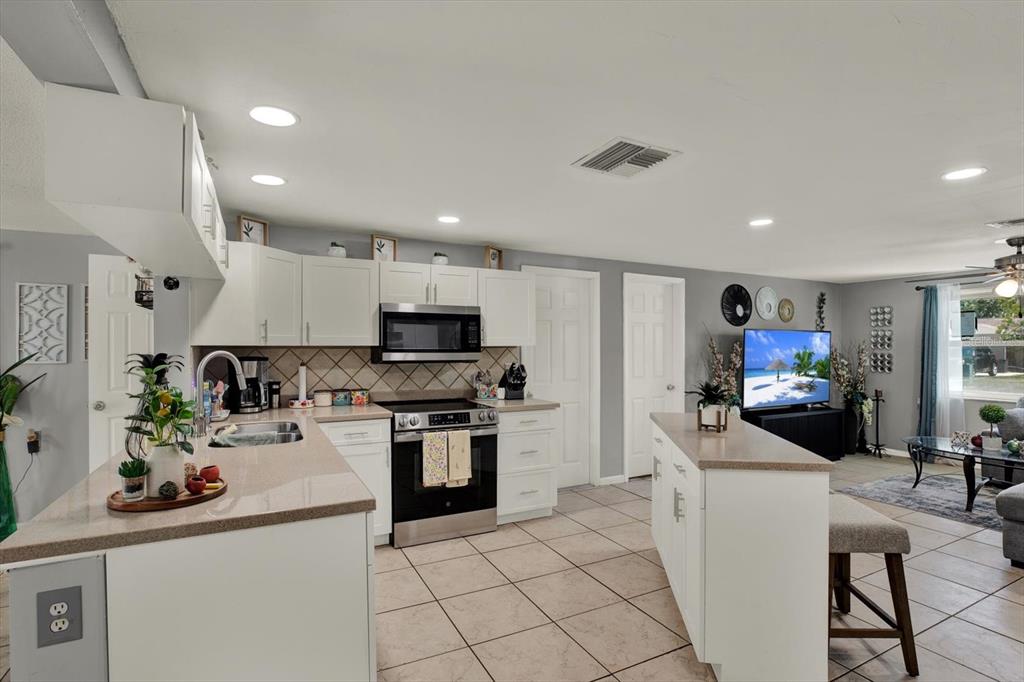 A kitchen with white cabinets, quartz countertops, and tile flooring opens into a living area — 5609 QUIST DRIVE, PORT RICHEY, FL