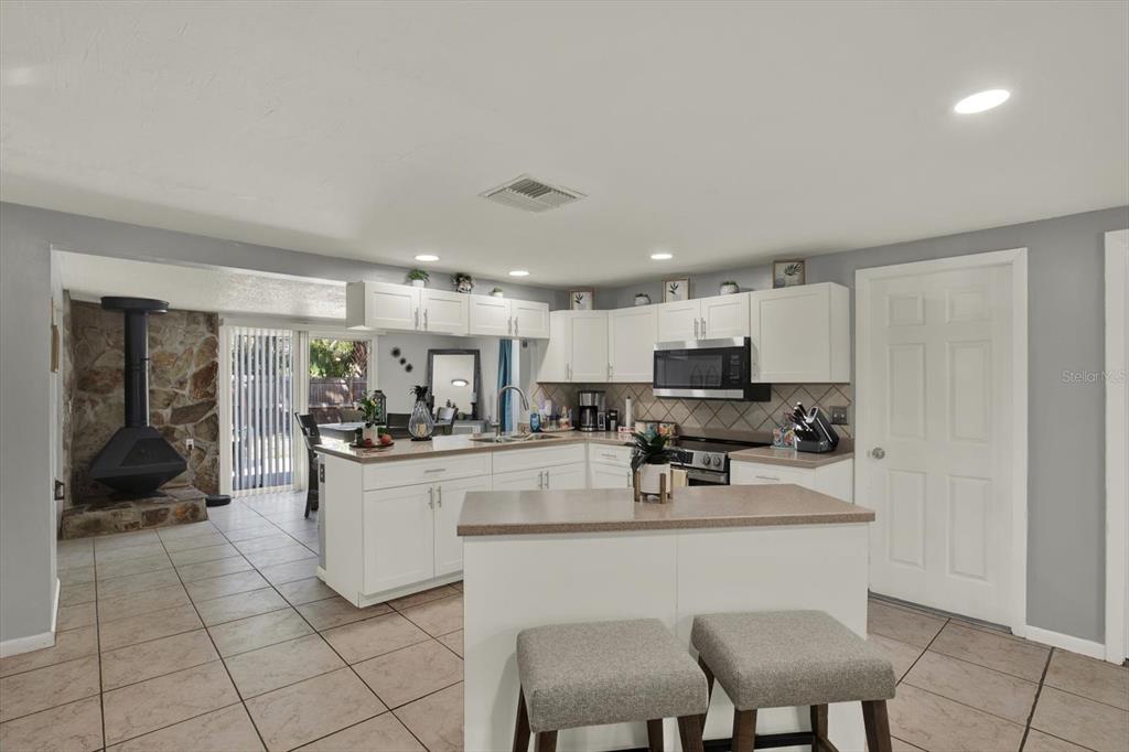 A kitchen features white cabinets, a central island with two stools, and tile flooring — 5609 QUIST DRIVE, PORT RICHEY, FL