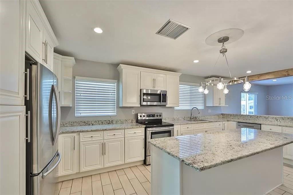 An open-concept kitchen and living area feature wood-look flooring and a rustic ceiling beam — 3219 W LEROY STREET, TAMPA, FL