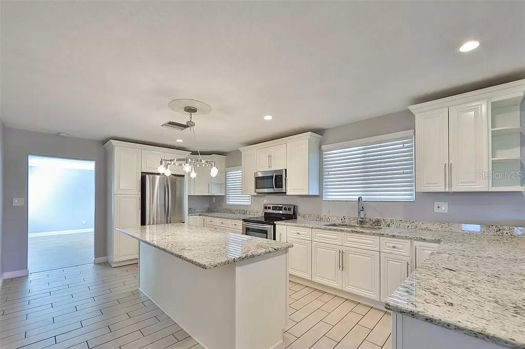 A kitchen features white cabinets, granite countertops, stainless steel appliances, and a pendant chandelier — 3219 W LEROY STREET, TAMPA, FL