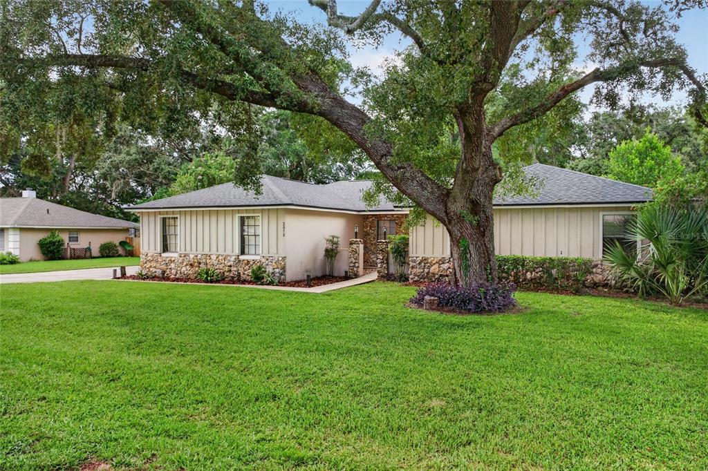 A single-story house with stone accents and vertical siding sits behind a large oak tree — 2070 SE 50TH TERRACE, OCALA, FL