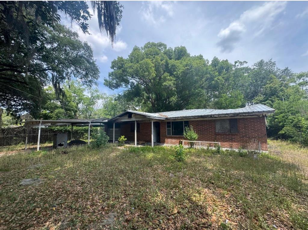 A single-story brick house with a metal roof and an attached carport sits on overgrown land — 8321 OLD PLANK ROAD, JACKSONVILLE, FL