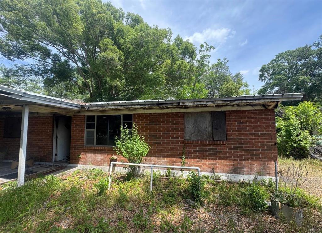 A single-story brick house with a metal roof and boarded-up windows sits in overgrown vegetation — 8321 OLD PLANK ROAD, JACKSONVILLE, FL