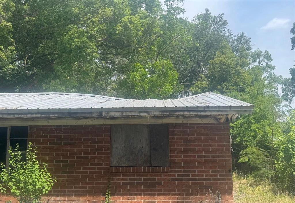 A brick house exterior features a sagging metal roof and a boarded-up window — 8321 OLD PLANK ROAD, JACKSONVILLE, FL
