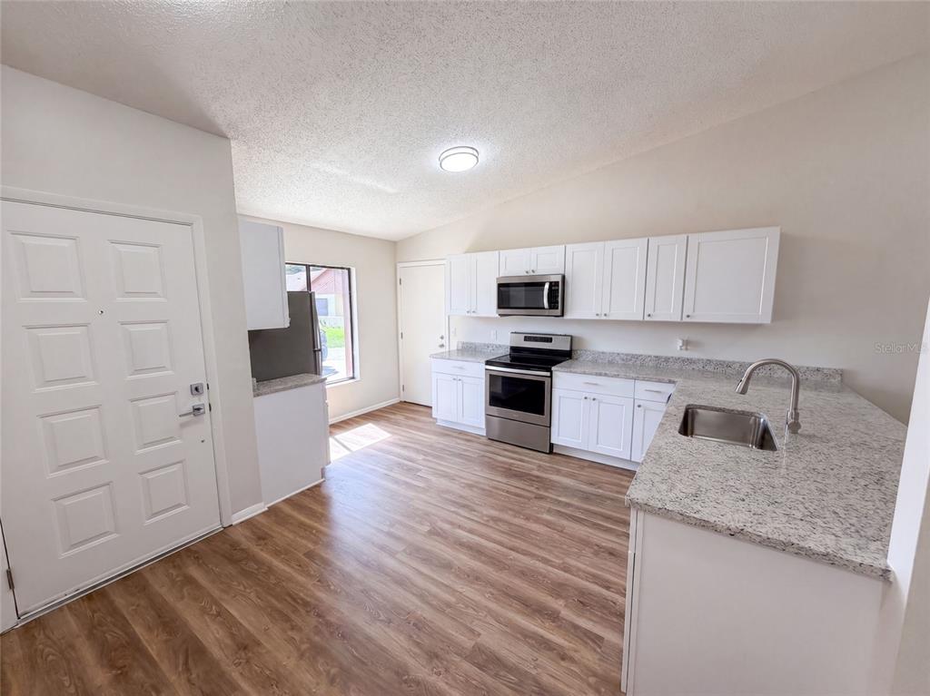 A kitchen features white cabinets, granite countertops, stainless steel appliances, and wood-look flooring — 190 PINE KNOLL COURT, CASSELBERRY, FL