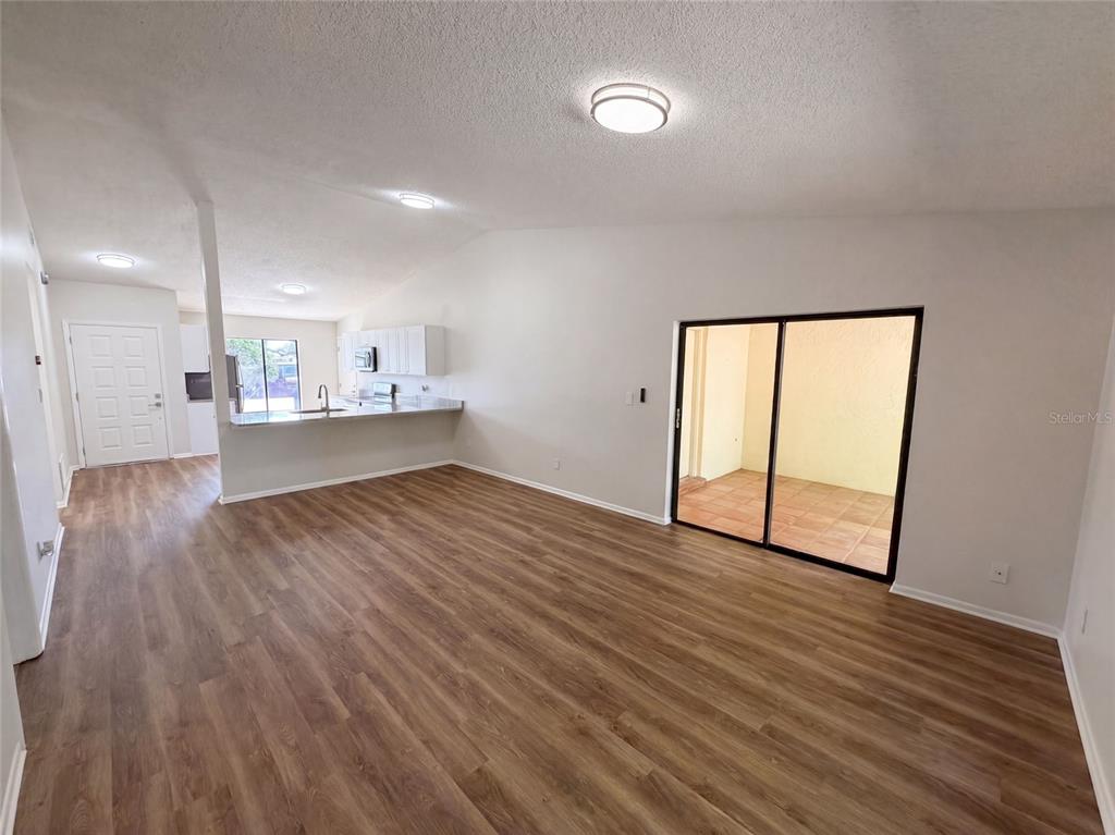 A living room with wood-look flooring, white walls, and a sliding glass door to a patio — 190 PINE KNOLL COURT, CASSELBERRY, FL