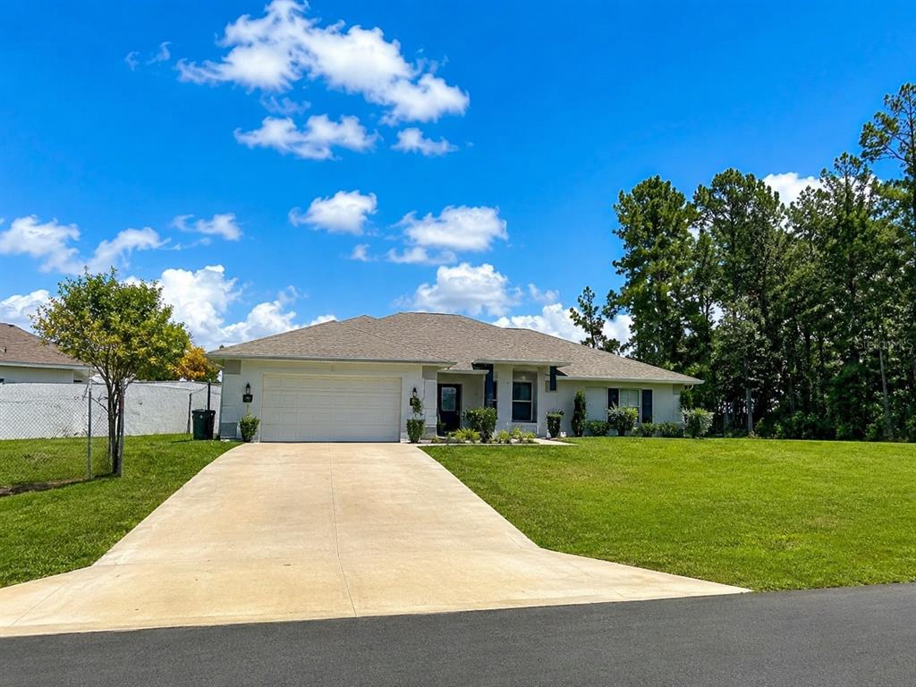 An open-concept living room features light blue walls, wood-look flooring, and a large area rug — 15329 SW 65TH TERRACE ROAD, OCALA, FL