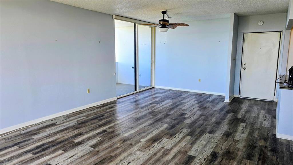 An empty living room features light blue walls, wood-look flooring, a ceiling fan, and sliding doors — 30 TURNER STREET UNIT 704, CLEARWATER, FL