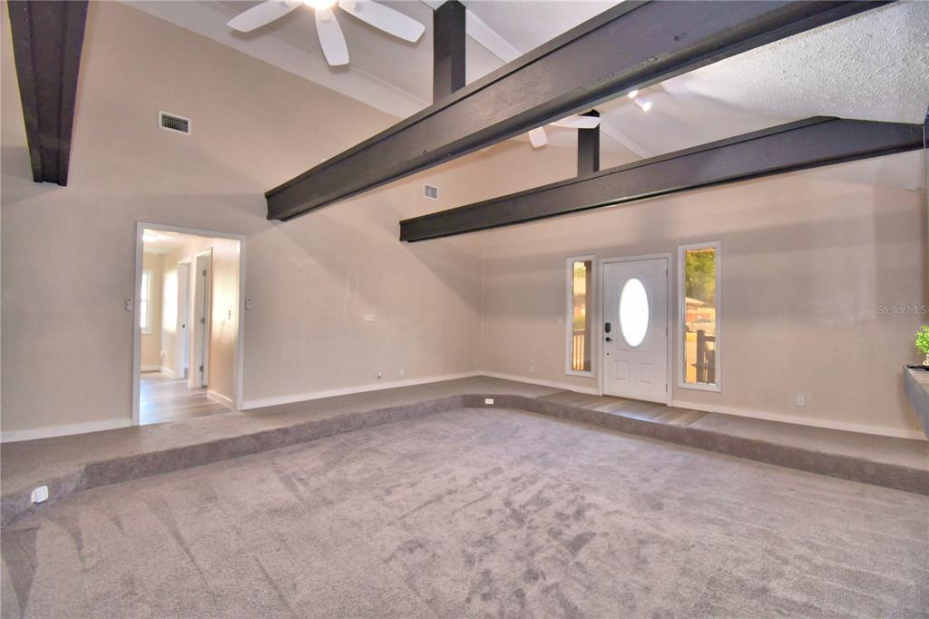 A sunken living room features dark exposed ceiling beams, gray carpeting, and a white door — 208 CENTER STREET, AUBURNDALE, FL
