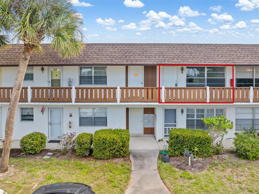 A two-story apartment building exterior features a wooden balcony and a red-outlined unit entrance — 2 QUAILS RUN BOULEVARD UNIT 8, ENGLEWOOD, FL
