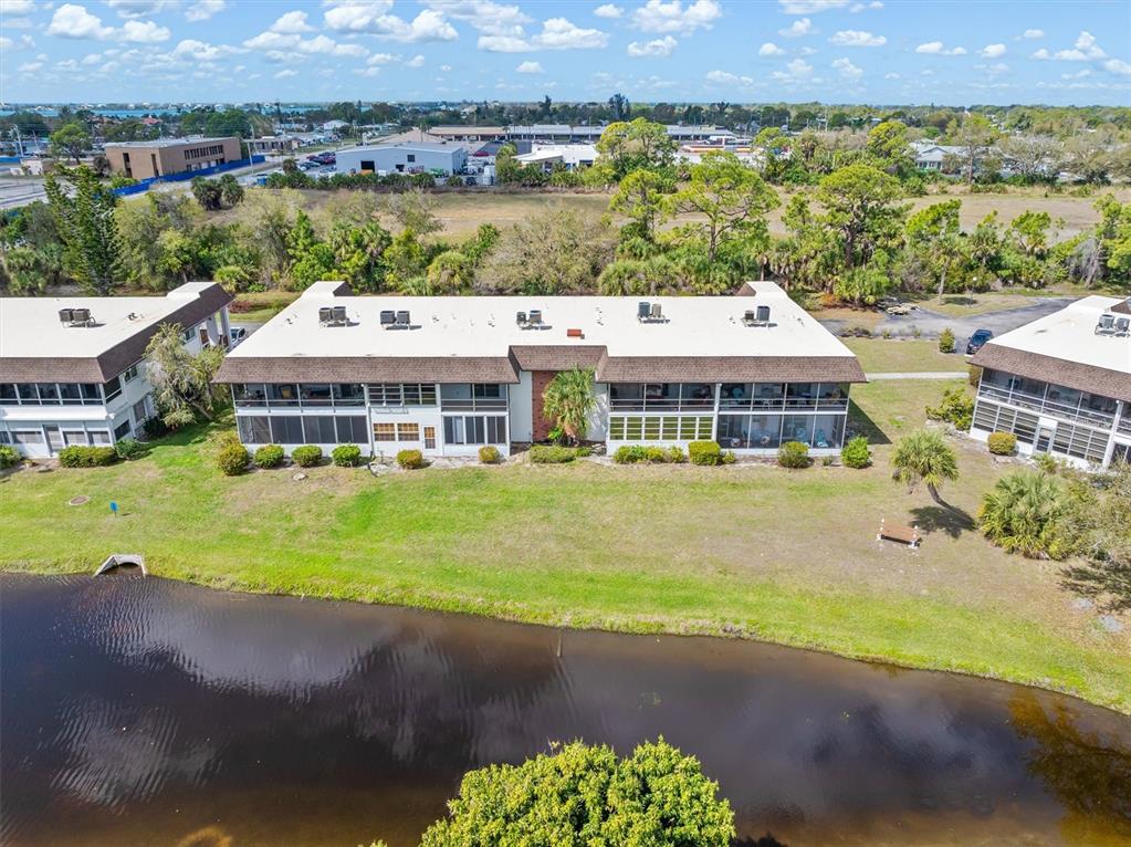 An aerial view shows a multi-story apartment building with a white roof beside a pond — 2 QUAILS RUN BOULEVARD UNIT 8, ENGLEWOOD, FL