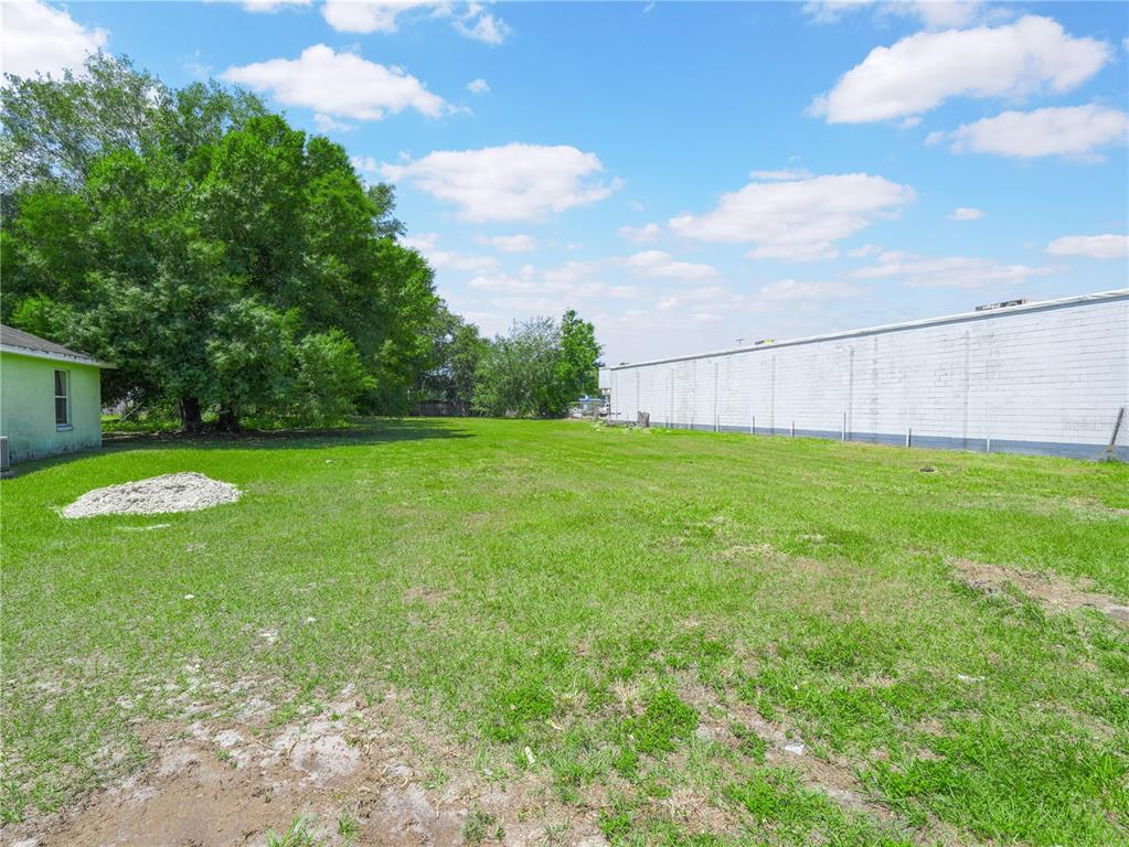 A grassy vacant lot sits between a small house and a long white building — LANIER AVENUE, FORT MEADE, FL